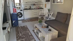A compact living space with a sofa, a coffee table, a washing machine, a microwave, and a dining area with chairs. - Casa Zimbo in Costa Calma (Pajara)