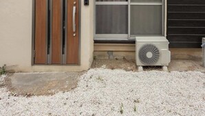 Une maison à deux étages avec une façade beige, une porte coulissante, une fenêtre avec des rideaux et un appareil de climatisation.