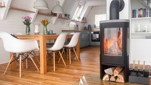 Une cuisine moderne avec un poêle à bois, un coin repas avec des chaises blanches et un plancher en bois.