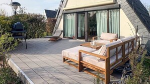 Une maison moderne avec un toit en pente, une terrasse dotée de mobilier d’extérieur et une grande porte-fenêtre coulissante.