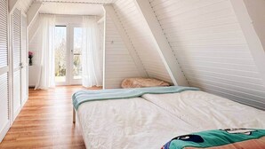Une chambre avec un plafond en pente, un lit avec des oreillers, une fenêtre avec des rideaux et un plancher en bois.