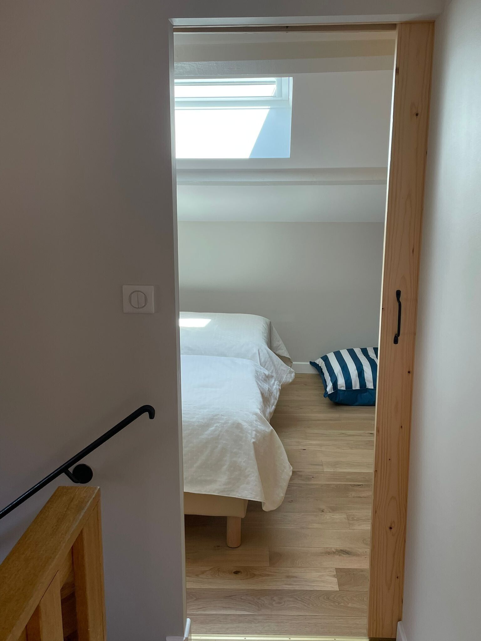 Ein enger Flur führt zu einem Schlafzimmer mit Bett, Fenster und Holzboden.
