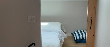 Un pasillo estrecho que conduce a un dormitorio con cama, ventana y suelo de madera.
