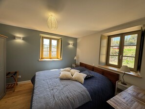 A bedroom with a bed, two windows, a bedside table, a lamp, and a wall-mounted light fixture. - Cottage “La Maison Du Potager” with Private Terrace and Garden (Laps)