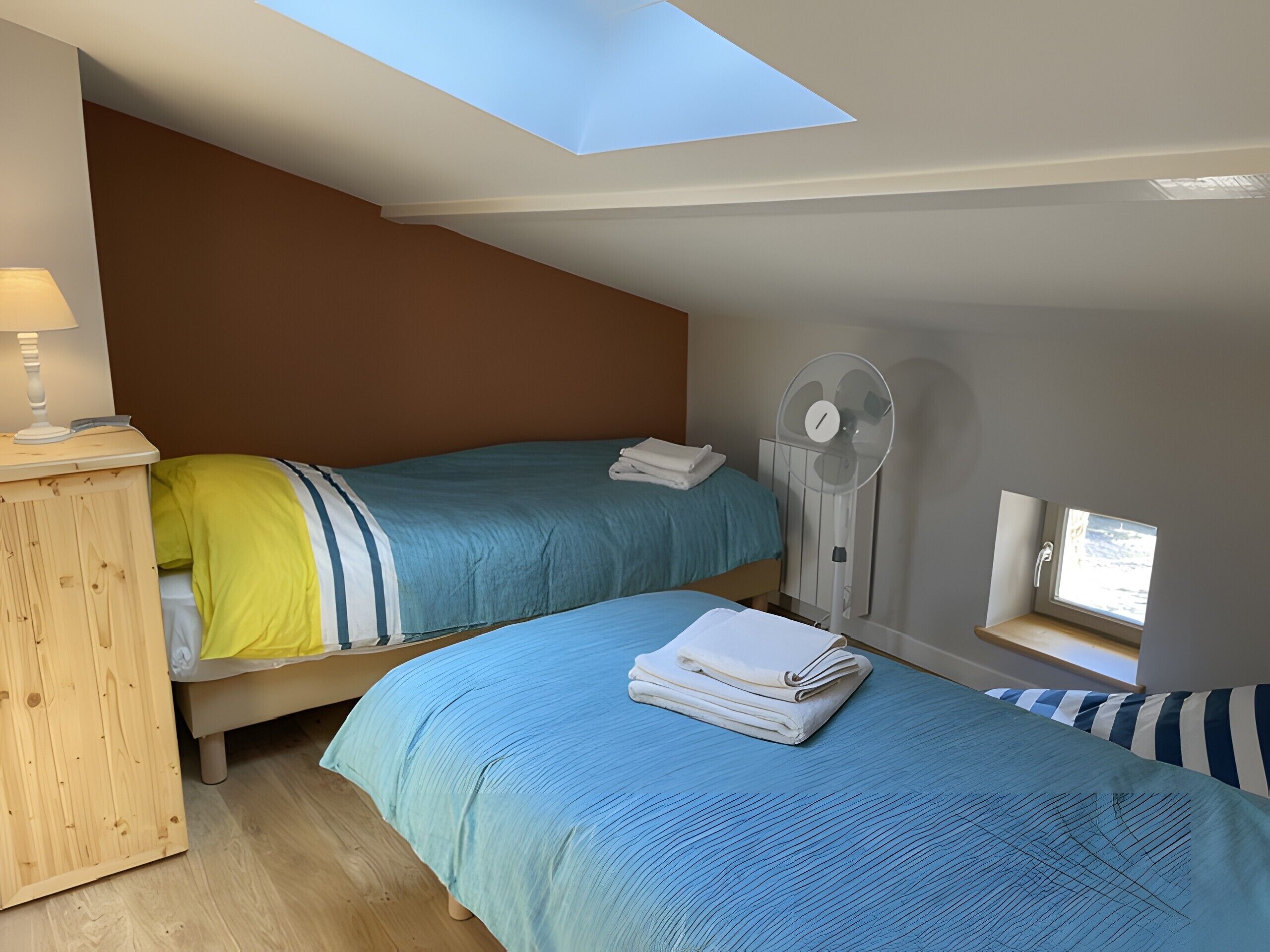 Un dormitorio con dos camas, un tragaluz, un ventilador y un ventanal pequeño.
