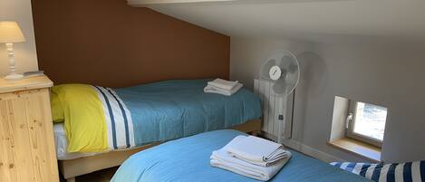 Un dormitorio con dos camas, un tragaluz, un ventilador y un ventanal pequeño.