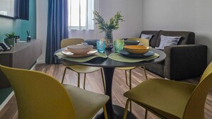 A modern living room with a dining table, chairs, a sofa, and a TV mounted on the wall. - Grey Pearl Suites - Green Pearl (Manfredonia)