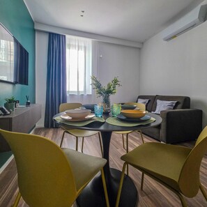 Una sala de estar moderna con una mesa de comedor, sillas, un sofá y un televisor montado en la pared.