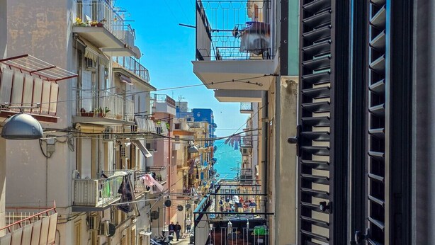 A narrow urban street flanked by multi-story buildings with balconies, a parked car, and a visible trash bin. - Grey Pearl Suites - Green Pearl (Manfredonia)