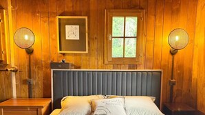 Ett rum med träpanel på väggarna, en säng, två sängbord, ett fönster och två vägglampor.