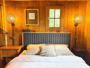 A wooden-paneled room with a bed, two nightstands, a window, and two wall-mounted lamps.