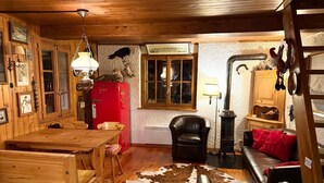 En rustik stuga med träinredning, ett rött kylskåp, en matta av kohud och en svart läderfåtölj.