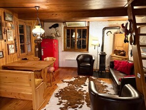 A rustic cabin interior with wooden furniture, a red refrigerator, a cowhide rug, and a black leather chair.