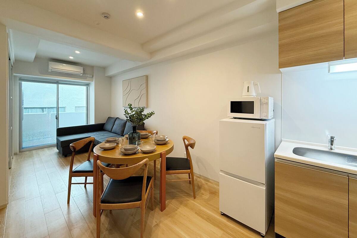 Una cocina moderna con microondas, refrigerador y comedor con sillas y mesa de madera.