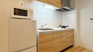 Cocina compacta con refrigerador blanco, microondas, gabinetes de madera, pileta de acero inoxidable y extractor moderno.