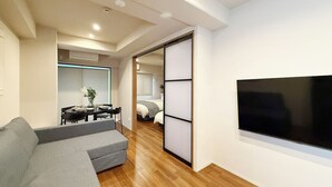 Una sala moderna con un sofá, una mesa de comedor con sillas, una cama con cabecera y un televisor montado en la pared.