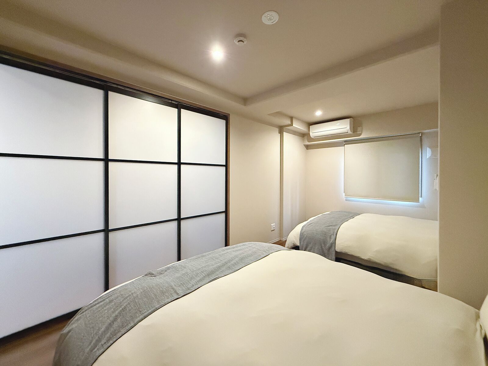 A bedroom with two beds, a sliding door, an air conditioning unit, and a window.