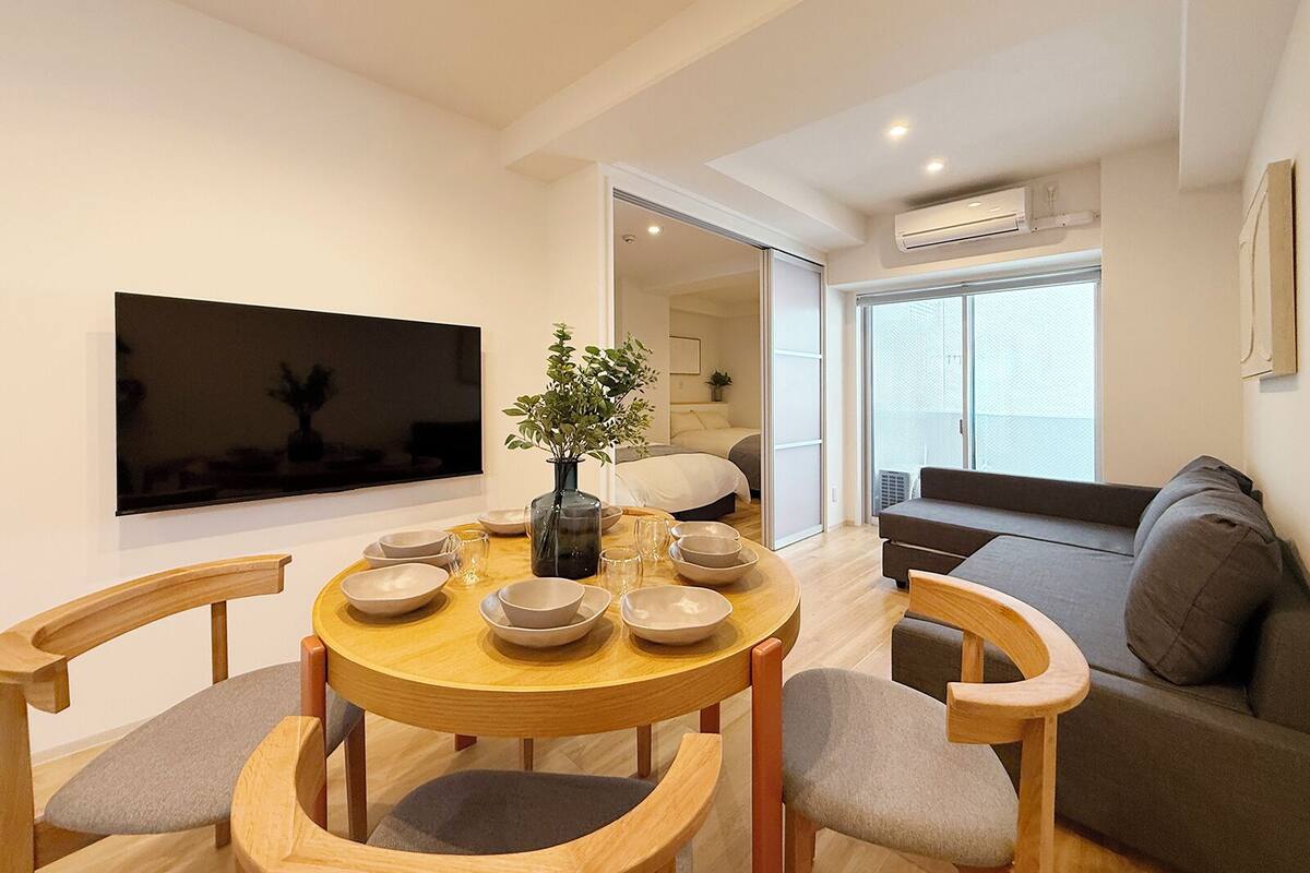 Una sala de estar moderna con una mesa de comedor redonda de madera, un sofá y un televisor montado en la pared.