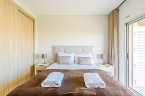 Ein Hotelzimmer mit einem großen Bett, zwei Nachttischen, einer Kopfteil und einem Fenster mit Vorhängen.