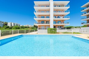 Ein modernes, mehrstöckiges Gebäude mit Balkonen, einem Schwimmbad und blauem Himmel.