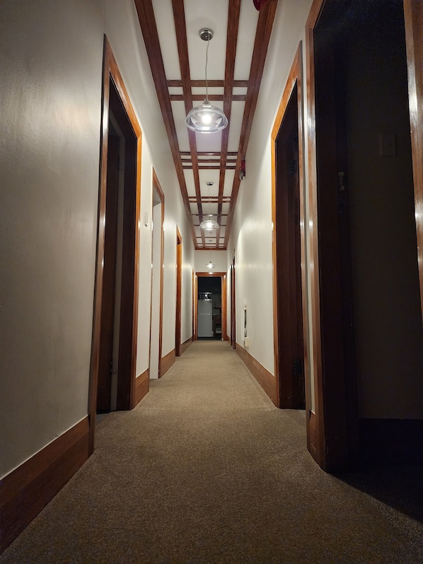 A hallway with wooden doors, a carpeted floor, and a ceiling with wooden beams and a hanging light fixture.