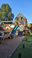 Una casita de juegos de madera con tobogán, pared de escalar y decoración de arcoíris.