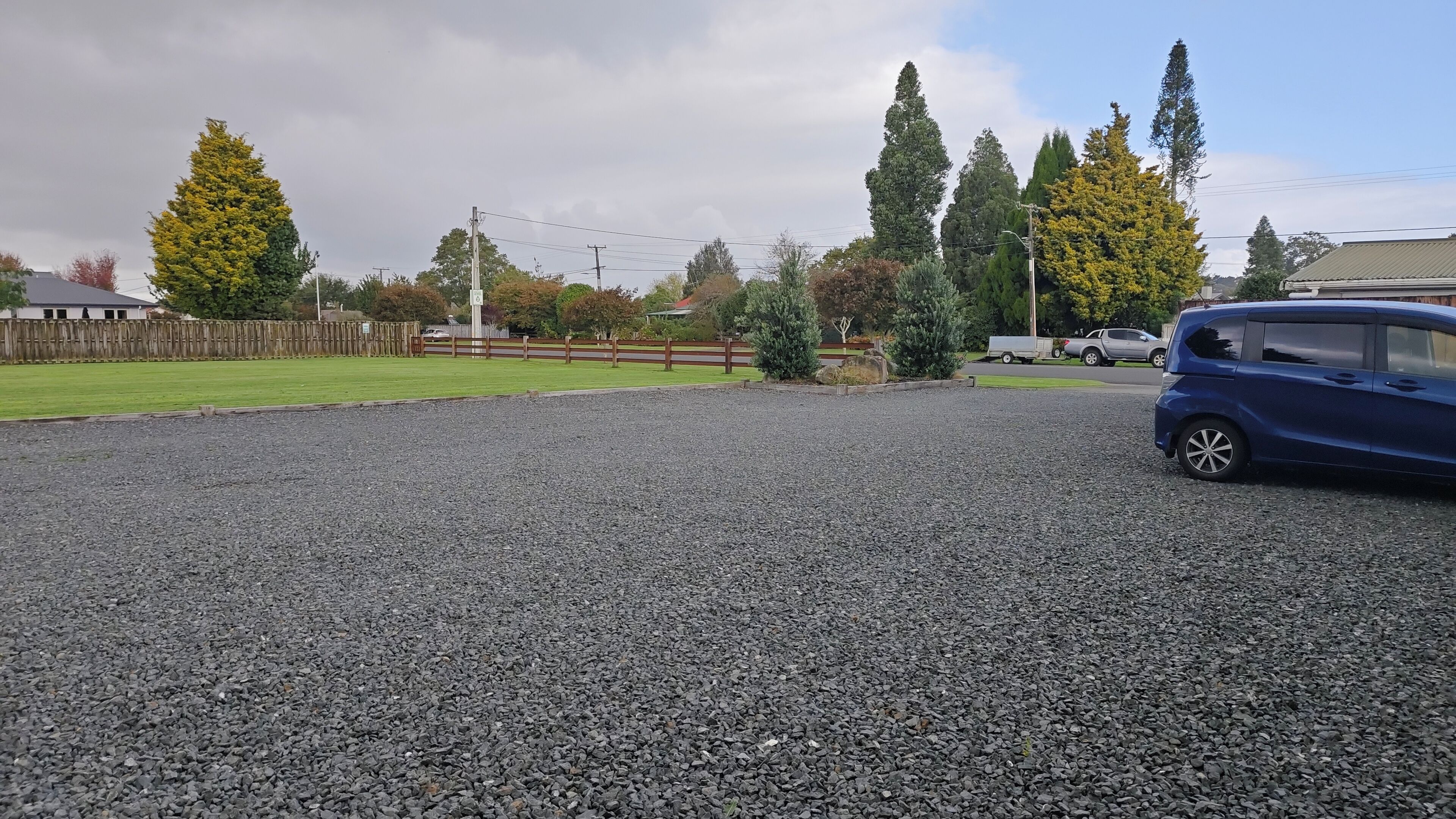 A gravel driveway, a blue car, and a wooden fence.