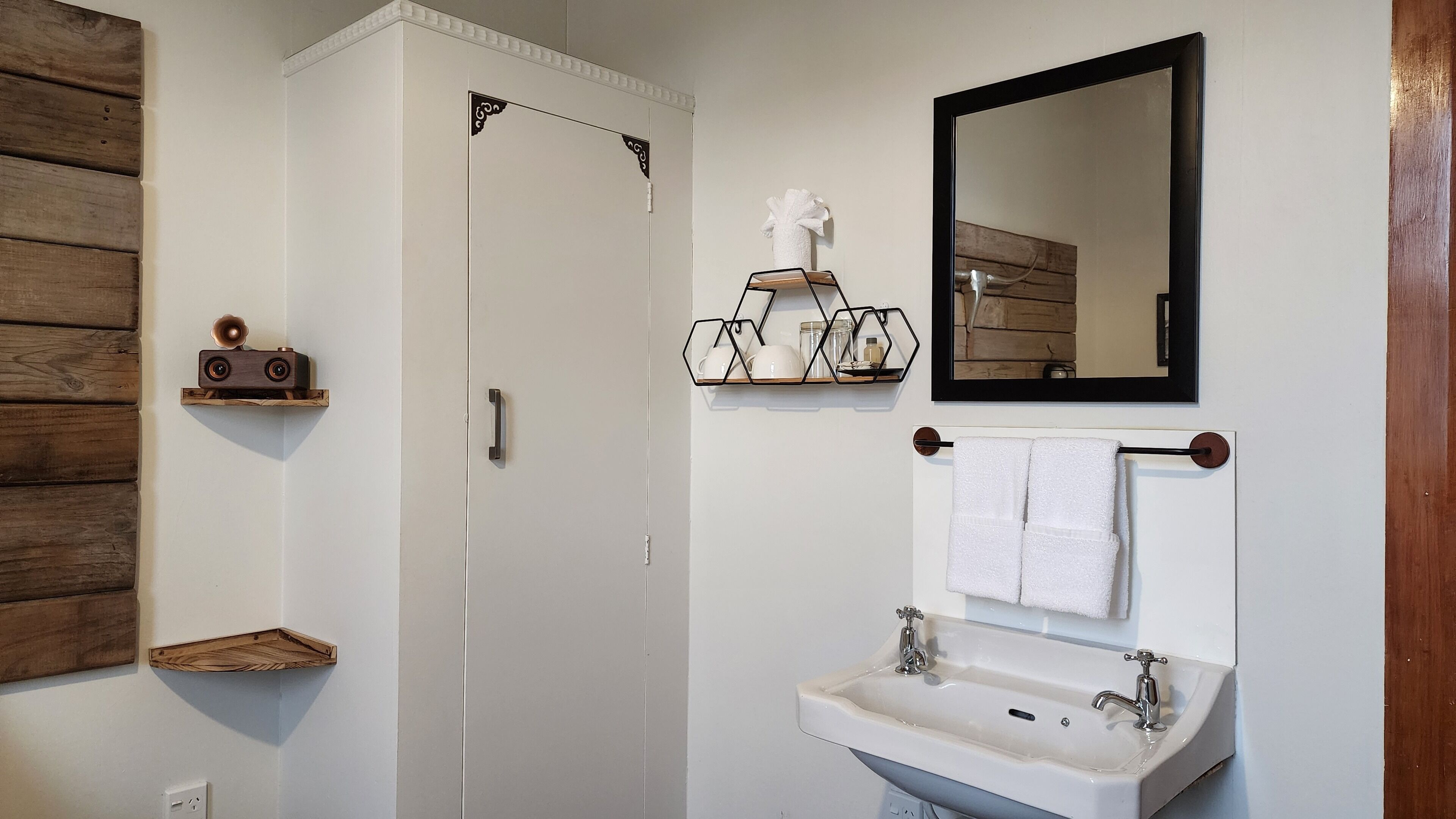 Een badkamer met een witte deur, een houten wandpaneel, een handdoekrek, een spiegel en een wastafel.
