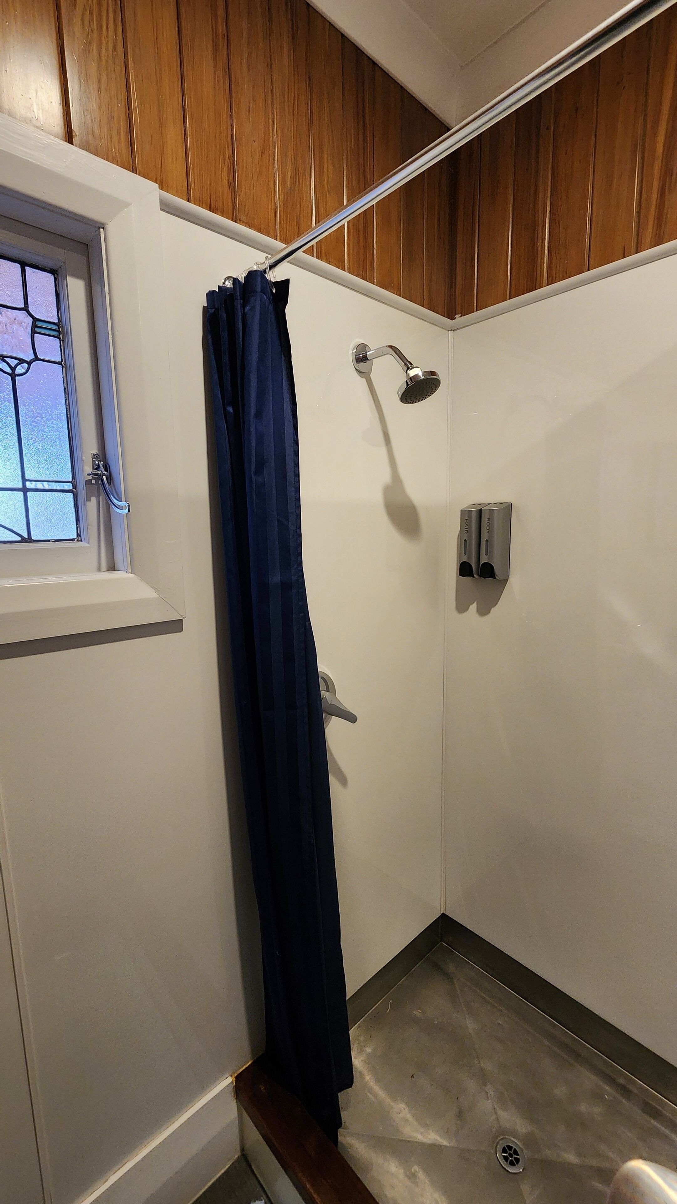 Ducha con cabezal de ducha de mano, cortina y ventana con un diseño de vitral.
