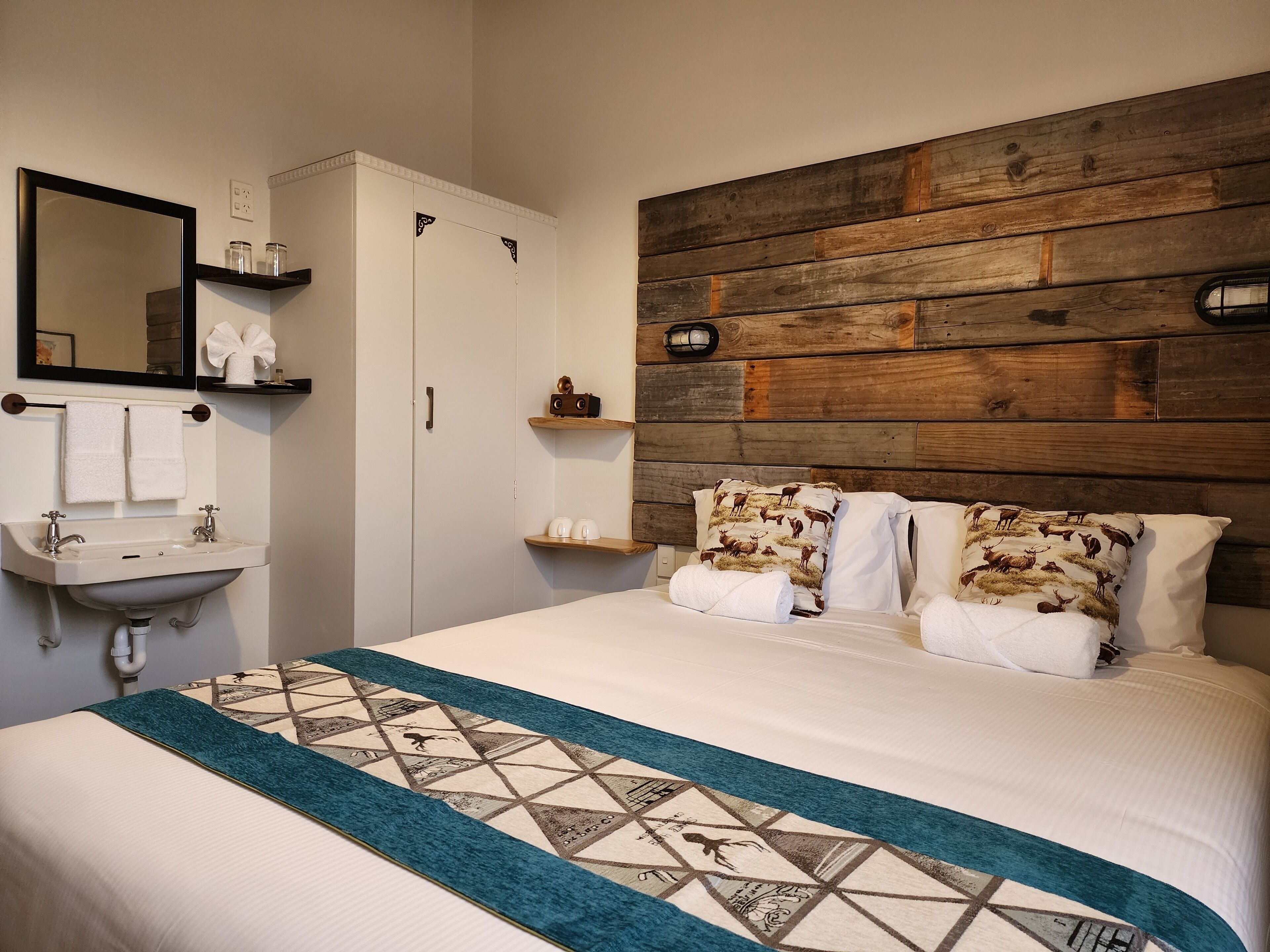 Un dormitorio con cama, mesita de noche, espejo, armario y lavamanos en el baño.