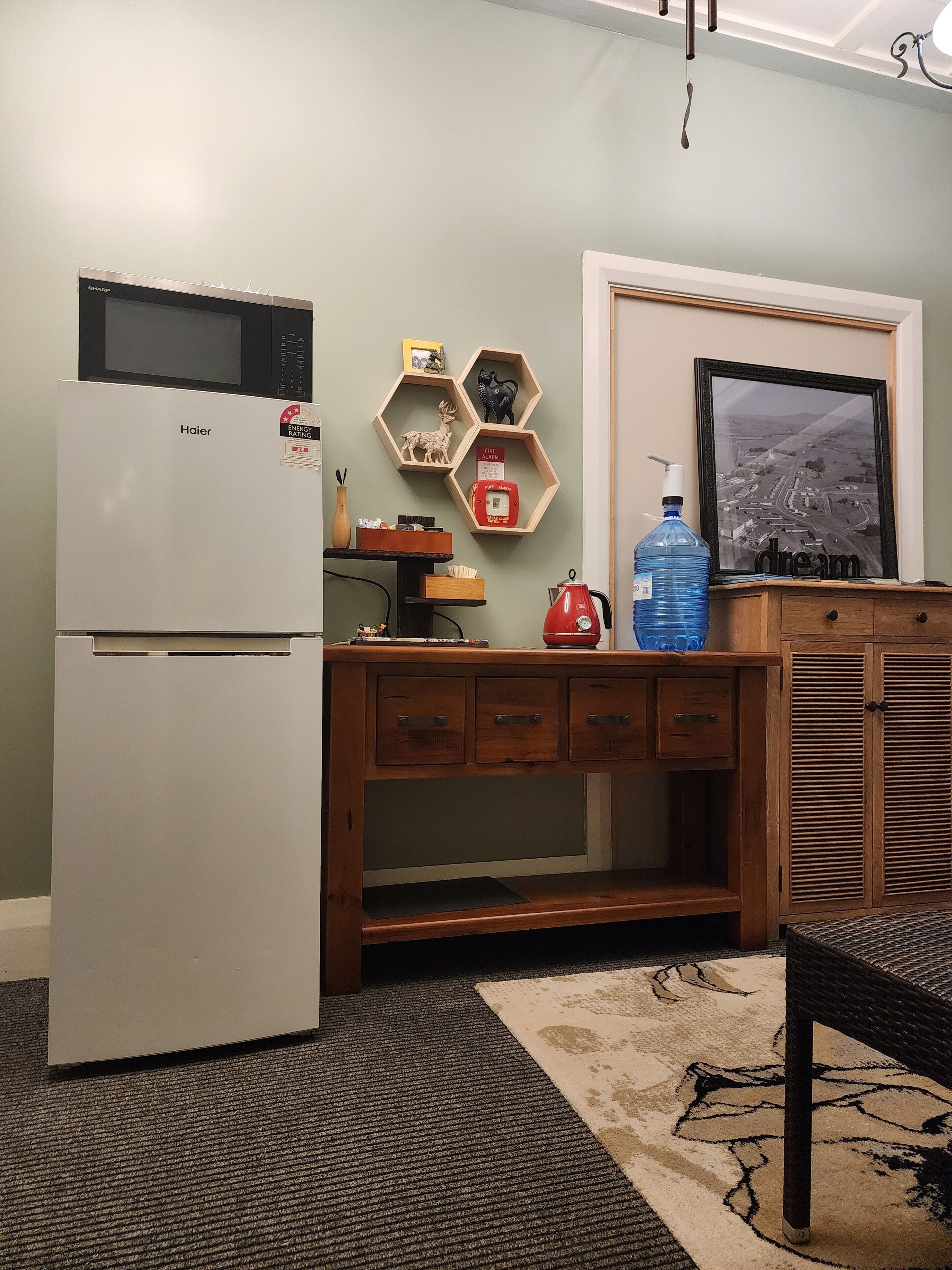 Una kitchenette compacta con refrigerador, cafetera, dispensador de agua y un cuadro en la pared.