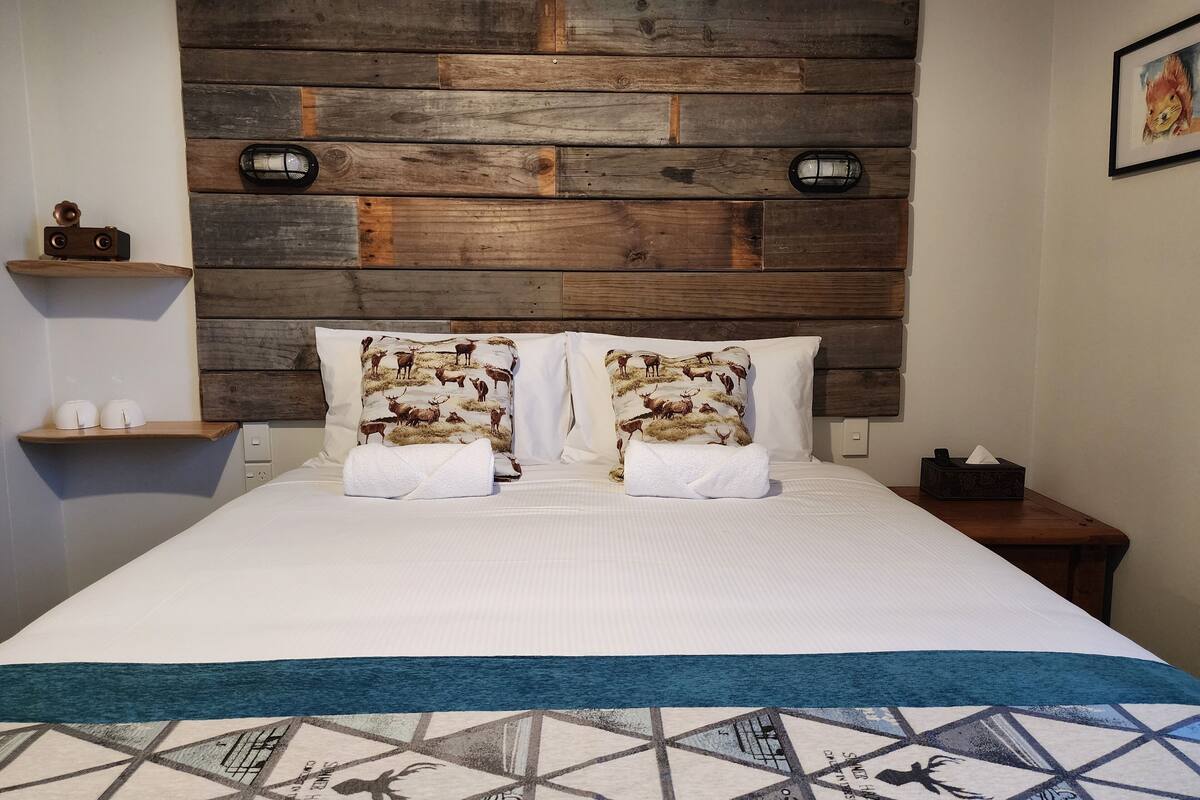 Un lit avec une tête de lit en bois, deux oreillers à motif de cerf, une couverture blanche et un plaid à motifs géométriques.