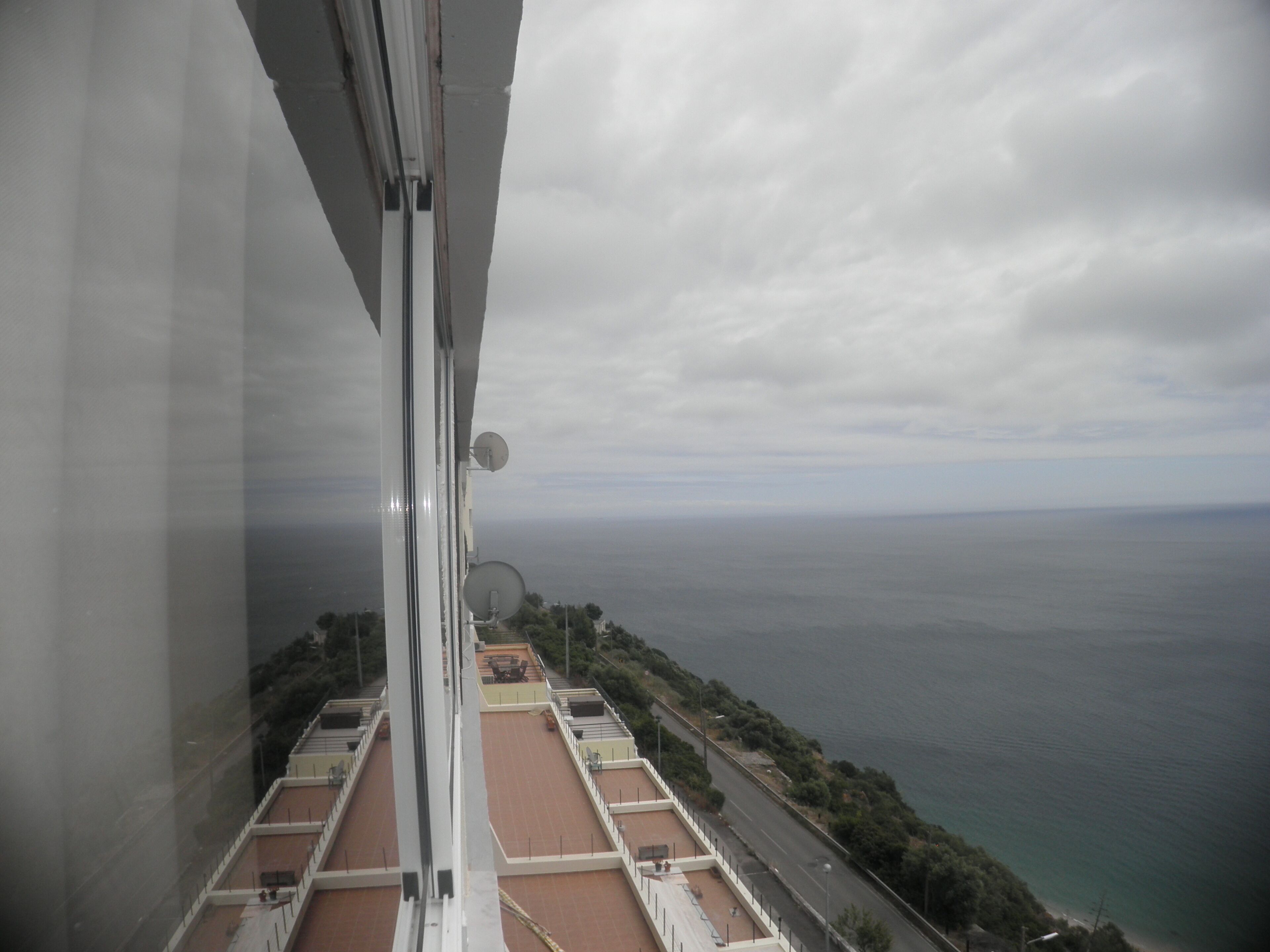 A high-rise building with a view of the sea and a road with greenery.
