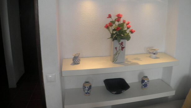 En hvid reol med en vase med røde blomster, en dekorativ skål og to små vaser med blå mønstre.