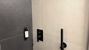 A bathroom with a shower, a bottle of shampoo, and a control panel. - Factory Suites (Prague)
