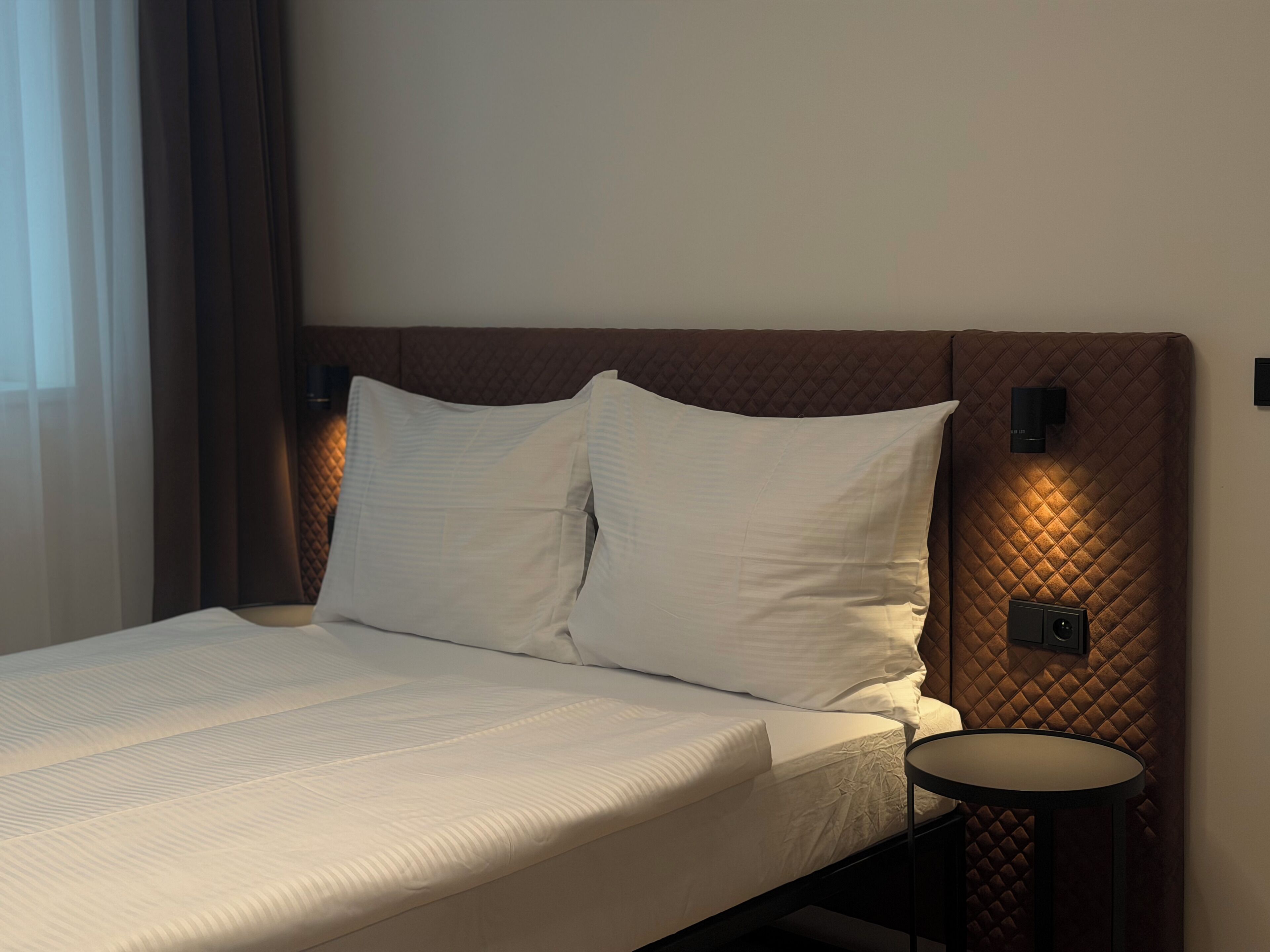 Habitación de hotel con cama, una mesita redonda y cabecera con iluminación integrada.