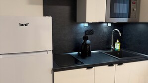 A modern kitchen with a refrigerator, microwave, sink, and black countertop. - Factory Suites (Prague)