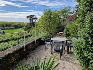 Eine Terrasse mit Tisch und Stühlen, umgeben von Pflanzen und einer Steinmauer.