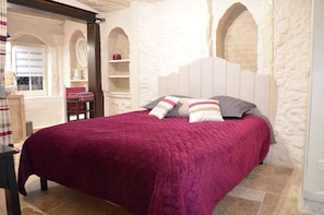 Ein Schlafzimmer mit einem Bett, einem Fenster, einem Spiegel und einem Regal mit Gegenständen.