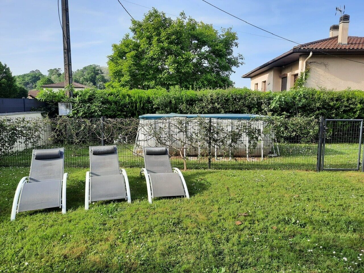 A grassy area with three lounge chairs and a fence.