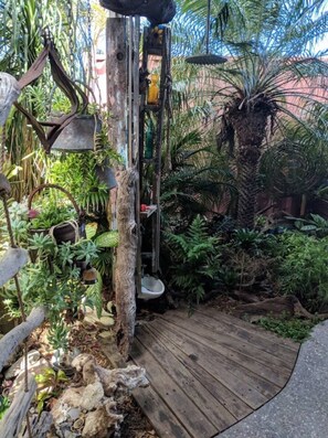 A rustic garden with a wooden deck, various plants, and a metal structure. - Salty Kisses Apartment. Across the road from the beach. (Marcoola)
