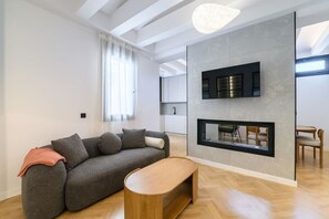 A modern living room with a sofa, a wooden coffee table, a fireplace, and a dining area with chairs. - 2BR 2BA | Almagro Residence | Quiet Luxury Stay (Madrid)