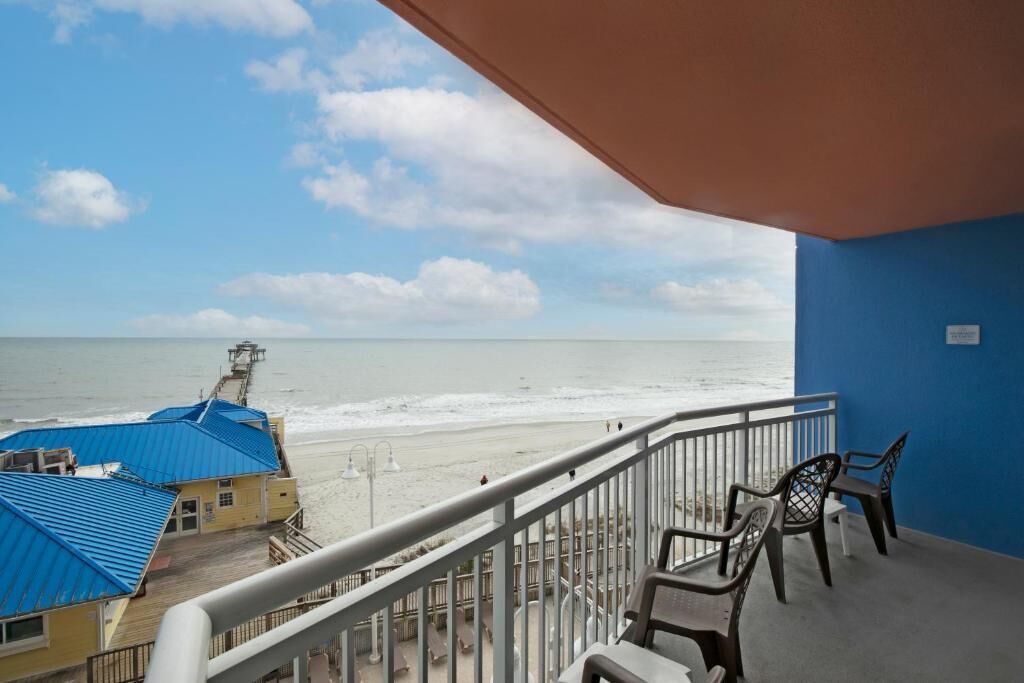 En balkon med udsigt over stranden og havet, en blå væg og et par stole.