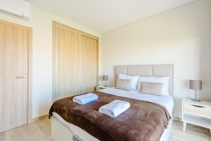 A bedroom with a bed, two bedside tables, a wardrobe, and an air conditioning unit. - Azul View Praia da Rocha (Portimão)
