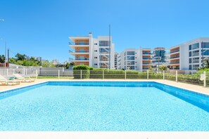 A swimming pool with a clear blue water surface, surrounded by a fence, and adjacent to modern multi-story buildings. - Azul View Praia da Rocha (Portimão)