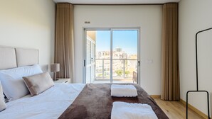 A hotel room with a large bed, a nightstand with a lamp, and a view of buildings through a sliding door. - Azul View Praia da Rocha (Portimão)