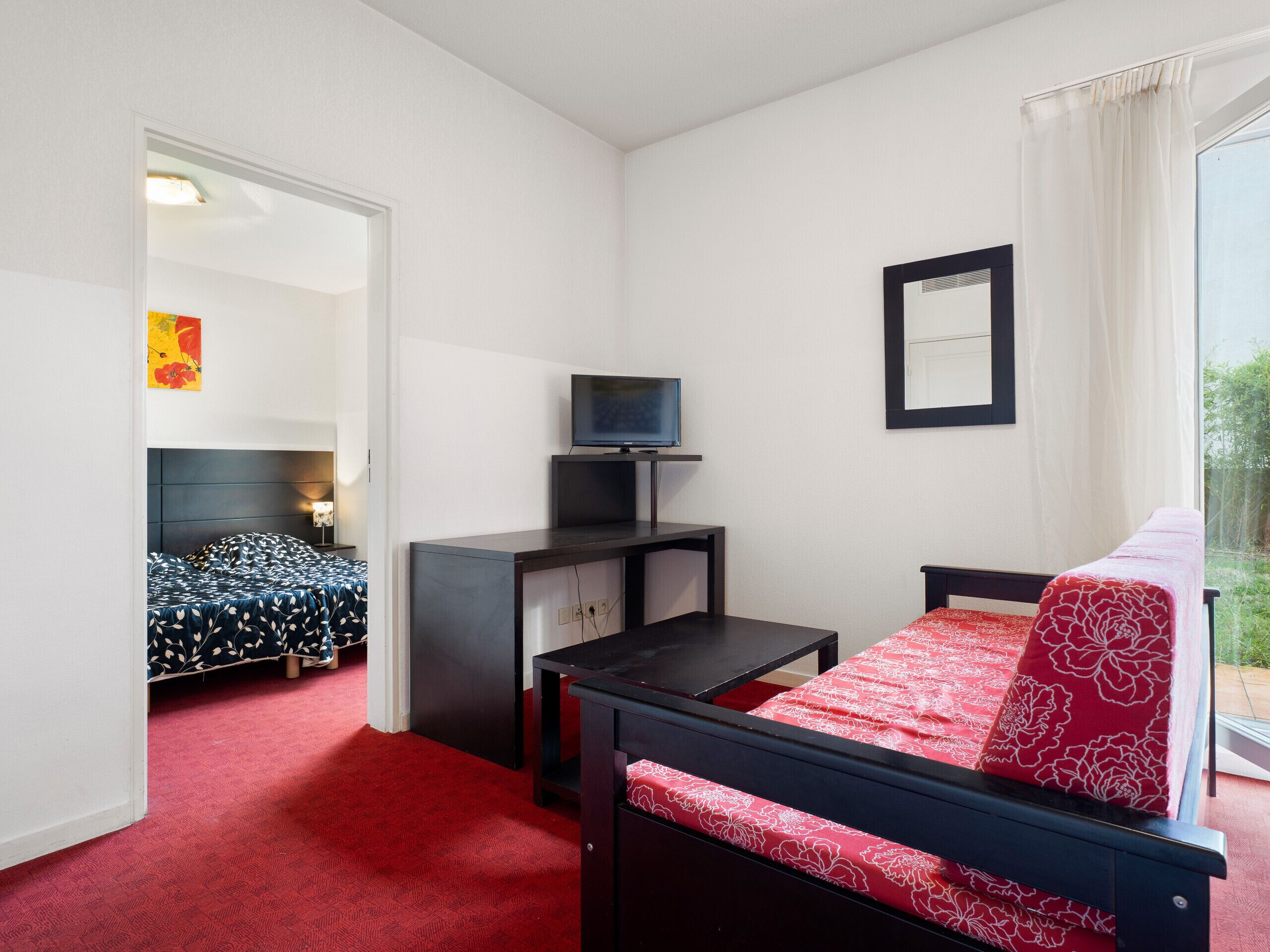 Une chambre avec un lit, un bureau, une télévision et une fenêtre avec des rideaux.