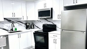 A modern kitchen with white cabinets, a black stove, a stainless steel refrigerator, and a microwave. - Private, Cozy, Luxury, Spacious One Bedroom Suite (Airdrie)