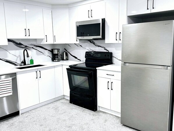 A modern kitchen with white cabinets, a black stove, a stainless steel refrigerator, and a microwave.