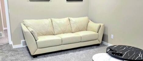 A living room with a beige sofa, a small round table, and two framed artworks on the wall.